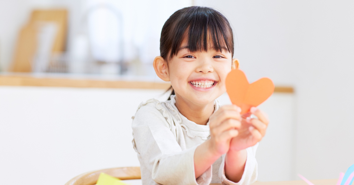 Girl smiling and holding up a heart art craft.
